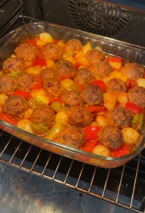 Baked meatballs with potatoes peppers and shallots in a glass baking dish in the oven