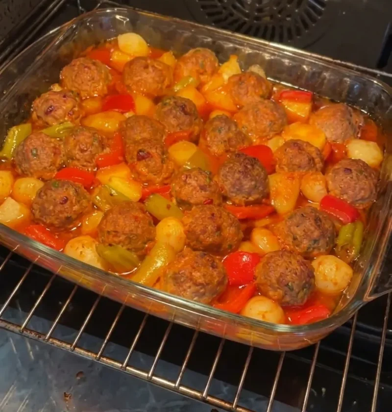Baked meatballs with potatoes peppers and shallots in a glass baking dish in the oven