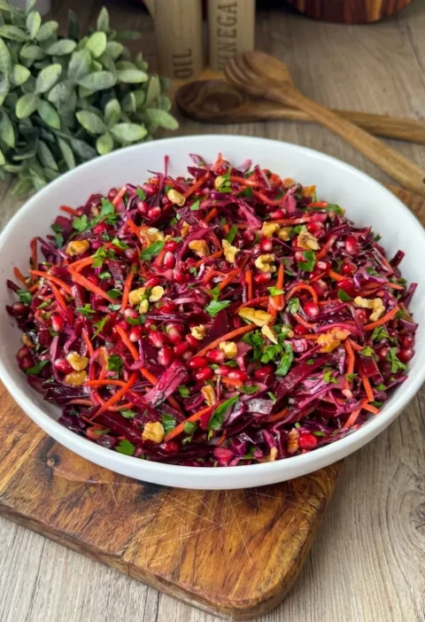 Beet and red cabbage salad with pomegranate seeds and walnuts in a white bowl