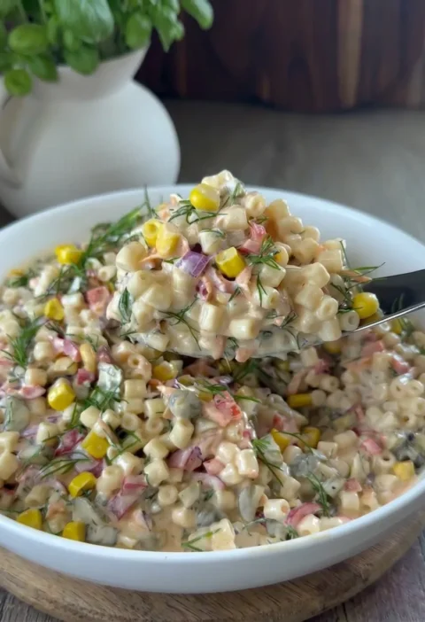 Creamy pasta salad with sweetcorn, red onion, pickles, and fresh dill in a white bowl