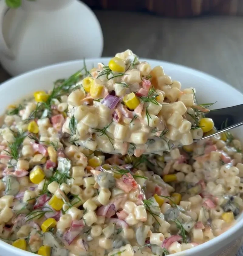 Creamy pasta salad with sweetcorn, red onion, pickles, and fresh dill in a white bowl