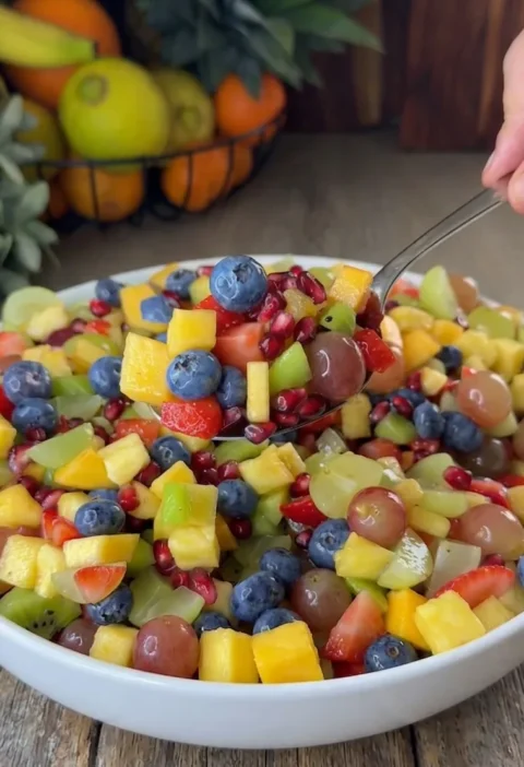 Easy honey lime fruit salad with mango strawberries kiwi blueberries grapes and pomegranate in a white bowl