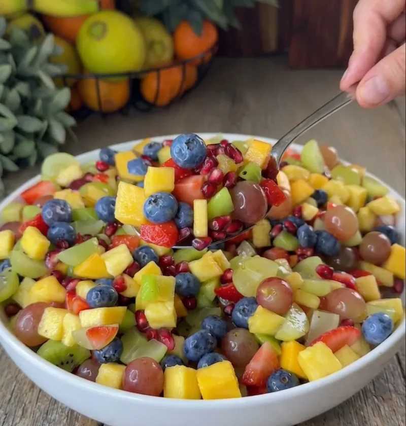 Easy honey lime fruit salad with mango strawberries kiwi blueberries grapes and pomegranate in a white bowl