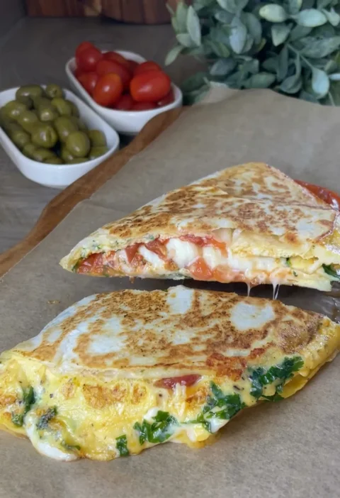 Egg and cheese breakfast quesadilla cut in half with melted cheese and fried tomatoes inside