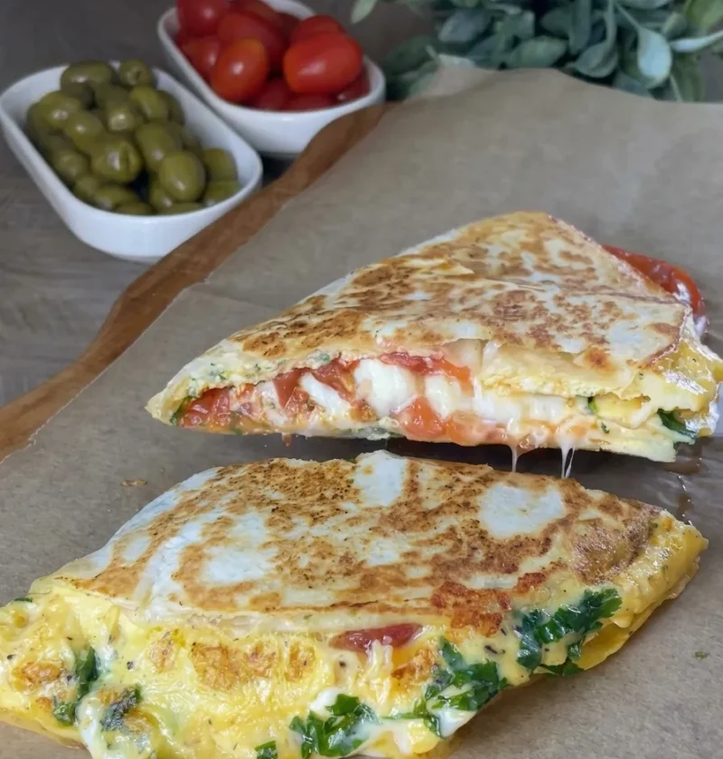 Egg and cheese breakfast quesadilla cut in half with melted cheese and fried tomatoes inside
