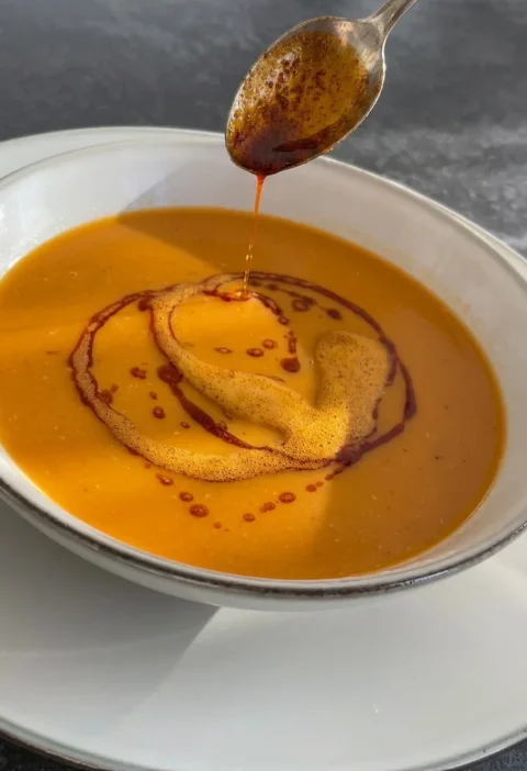 Red lentil soup in a white bowl with a spoon drizzling paprika butter on top
