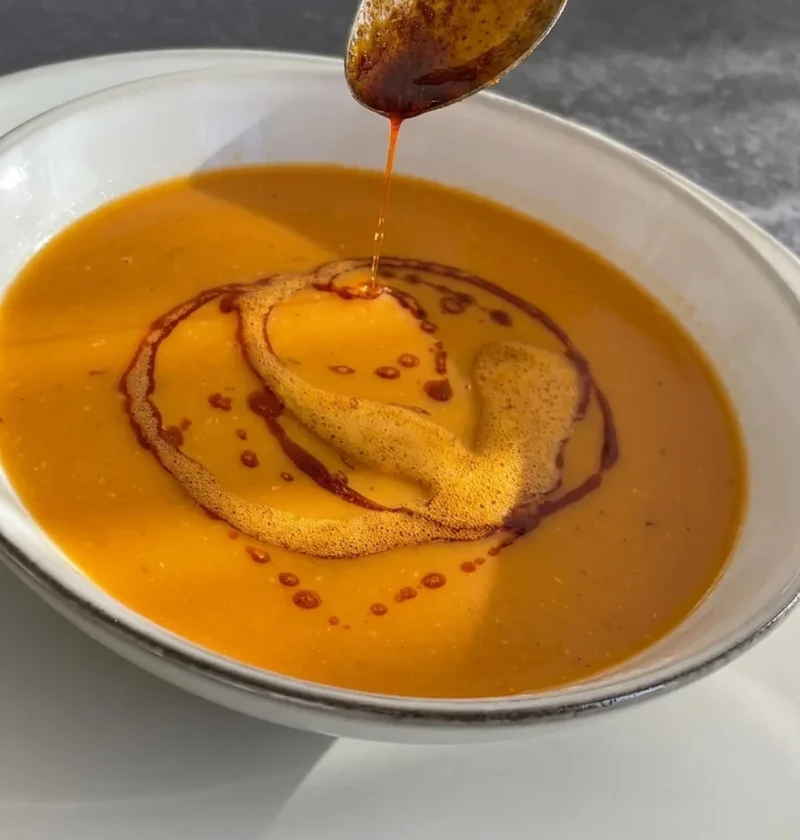 Red lentil soup in a white bowl with a spoon drizzling paprika butter on top