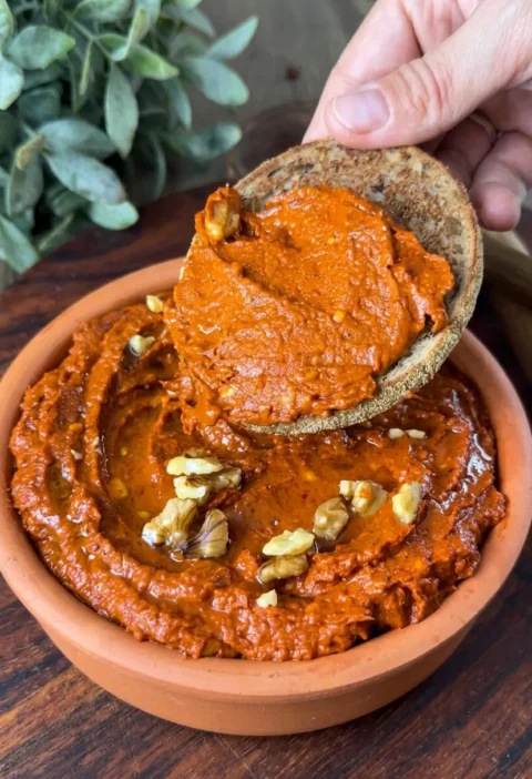 Spicy red pepper walnut dip spread thick on bread from a terracotta bowl