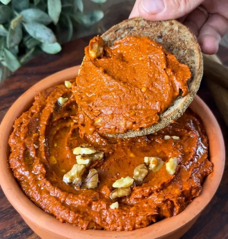 Spicy red pepper walnut dip spread thick on bread from a terracotta bowl
