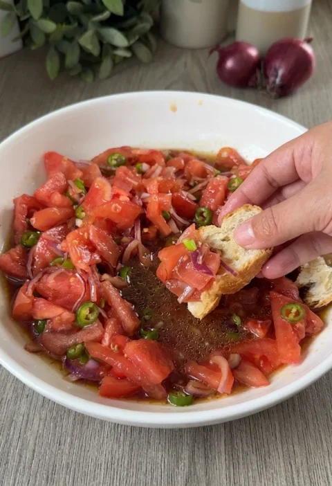 Tomato onion salad in a white bowl with soy sauce dressing and crusty bread for dipping