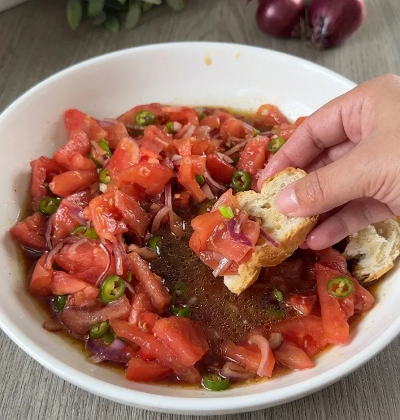 Tomato onion salad in a white bowl with soy sauce dressing and crusty bread for dipping